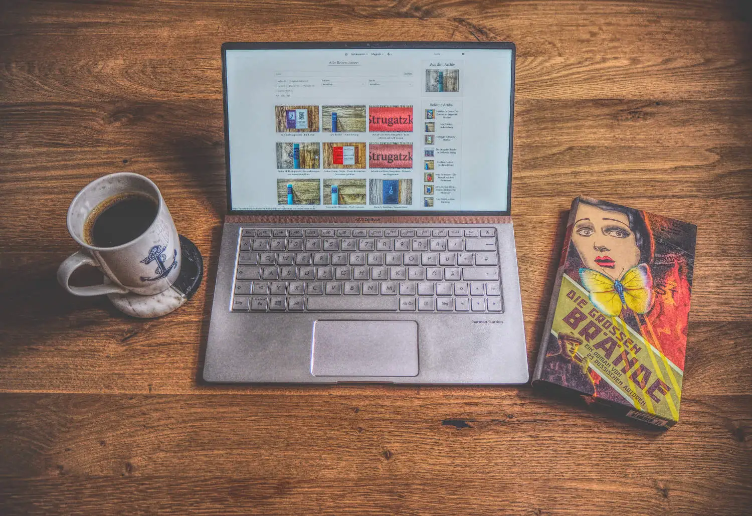 Ein Laptop mit einem Buch und einer Tasse Kaffee auf einem Holztisch.