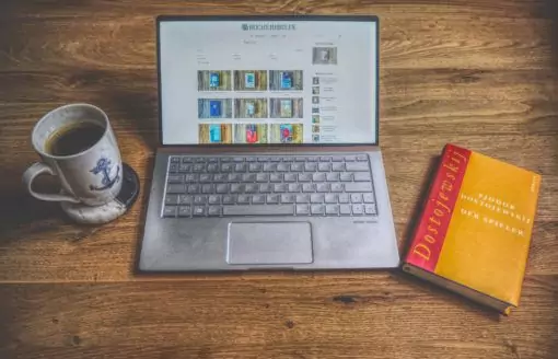 Ein Laptop mit einem Buch und einer Tasse Kaffee auf einem Holztisch.
