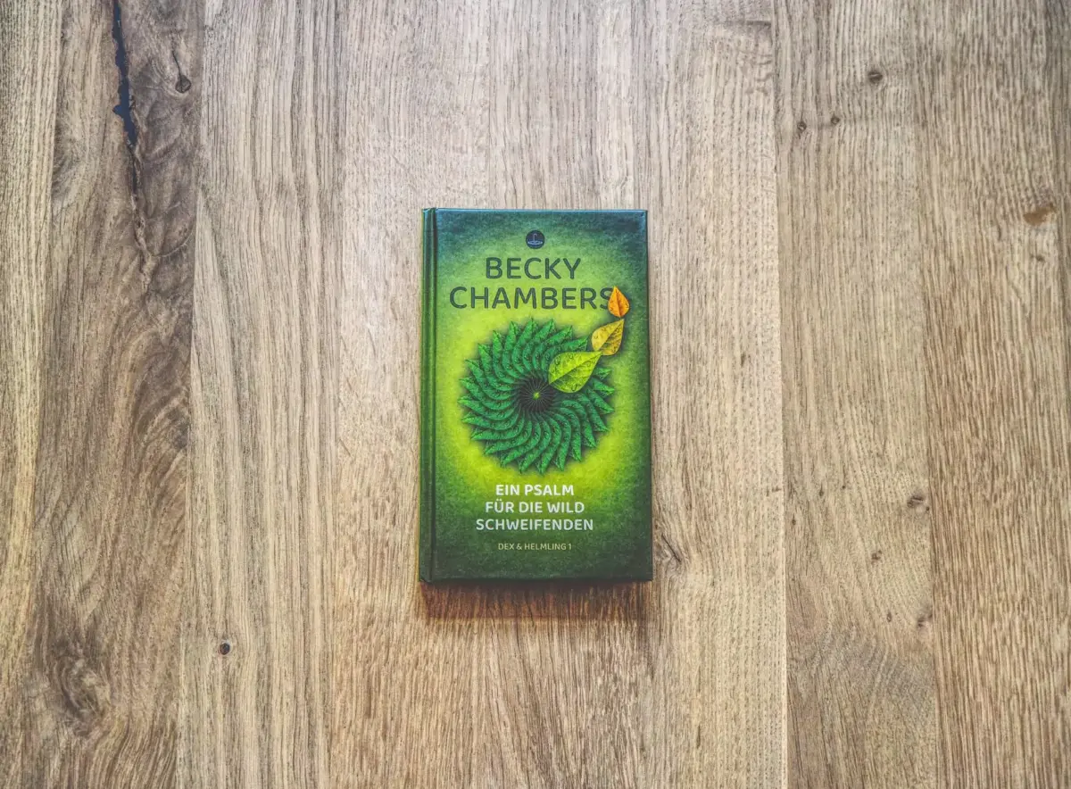 Auf einer Holzfläche liegt ein Buch mit dem Titel „Ein Psalm für die Wild Schweifenden“ von Becky Chambers.