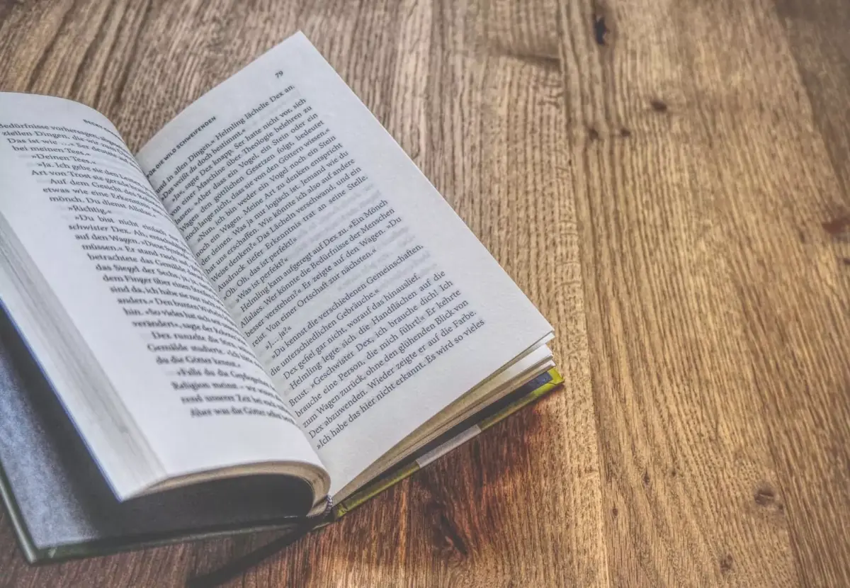Ein offenes Buch auf einem Holztisch, auf dessen Seiten sichtbarer Text mit einem unscharfen Hintergrund angezeigt wird.