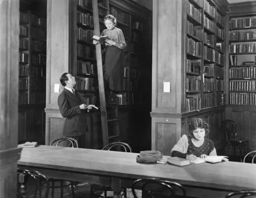 Ein Mann und eine Frau stehen in einer Bibliothek mit Bücherregalen.