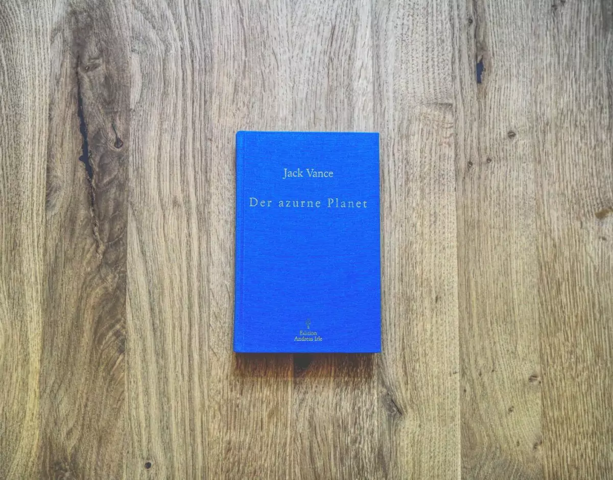 Ein blaues Buch mit dem Titel „Der azurne Planet“ von Jack Vance liegt auf einer Holzoberfläche.