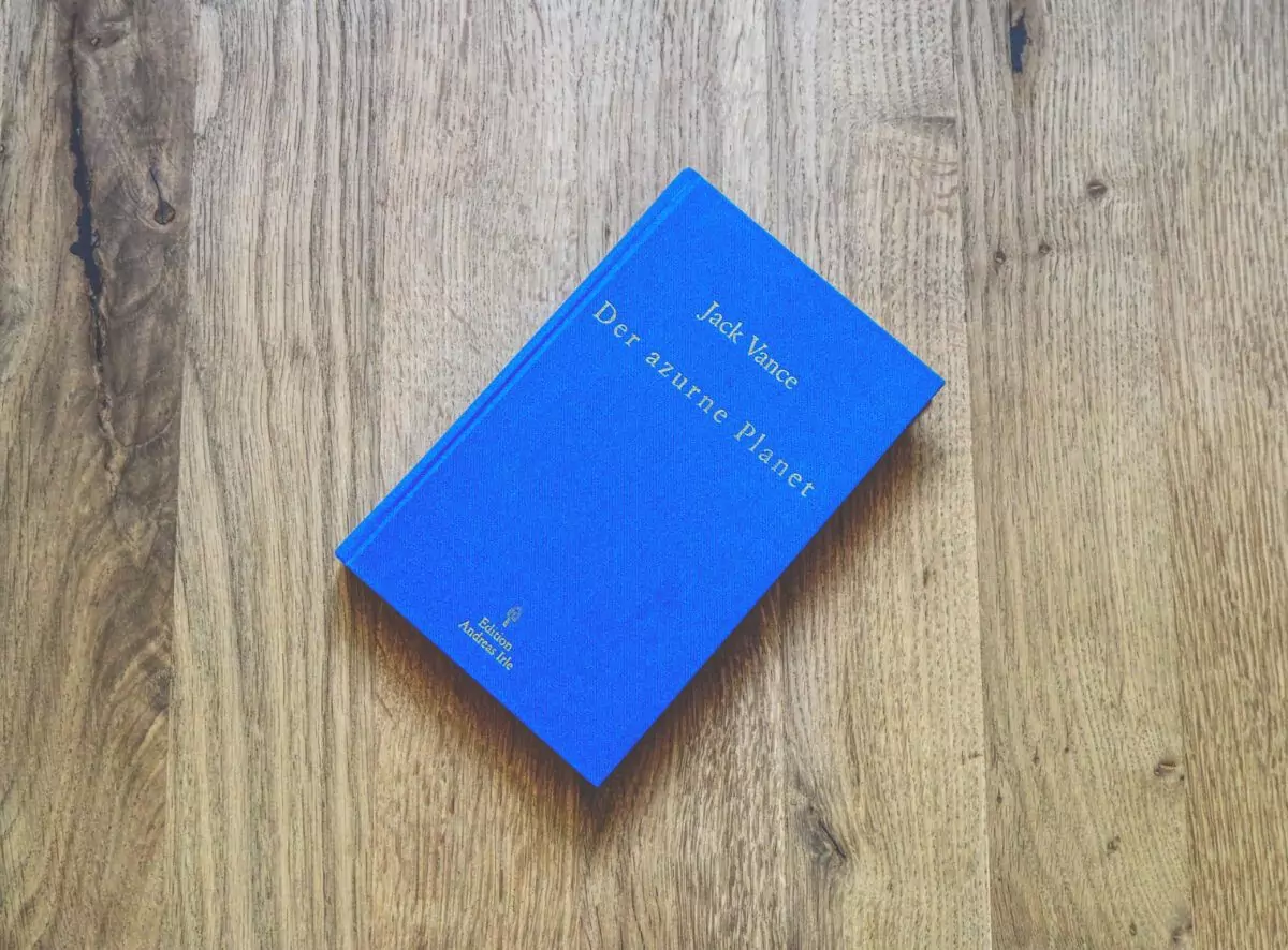 Ein blaues Buch mit dem Titel „Der azurblaue Planet“ von Jack Vance liegt auf einer Holzoberfläche.