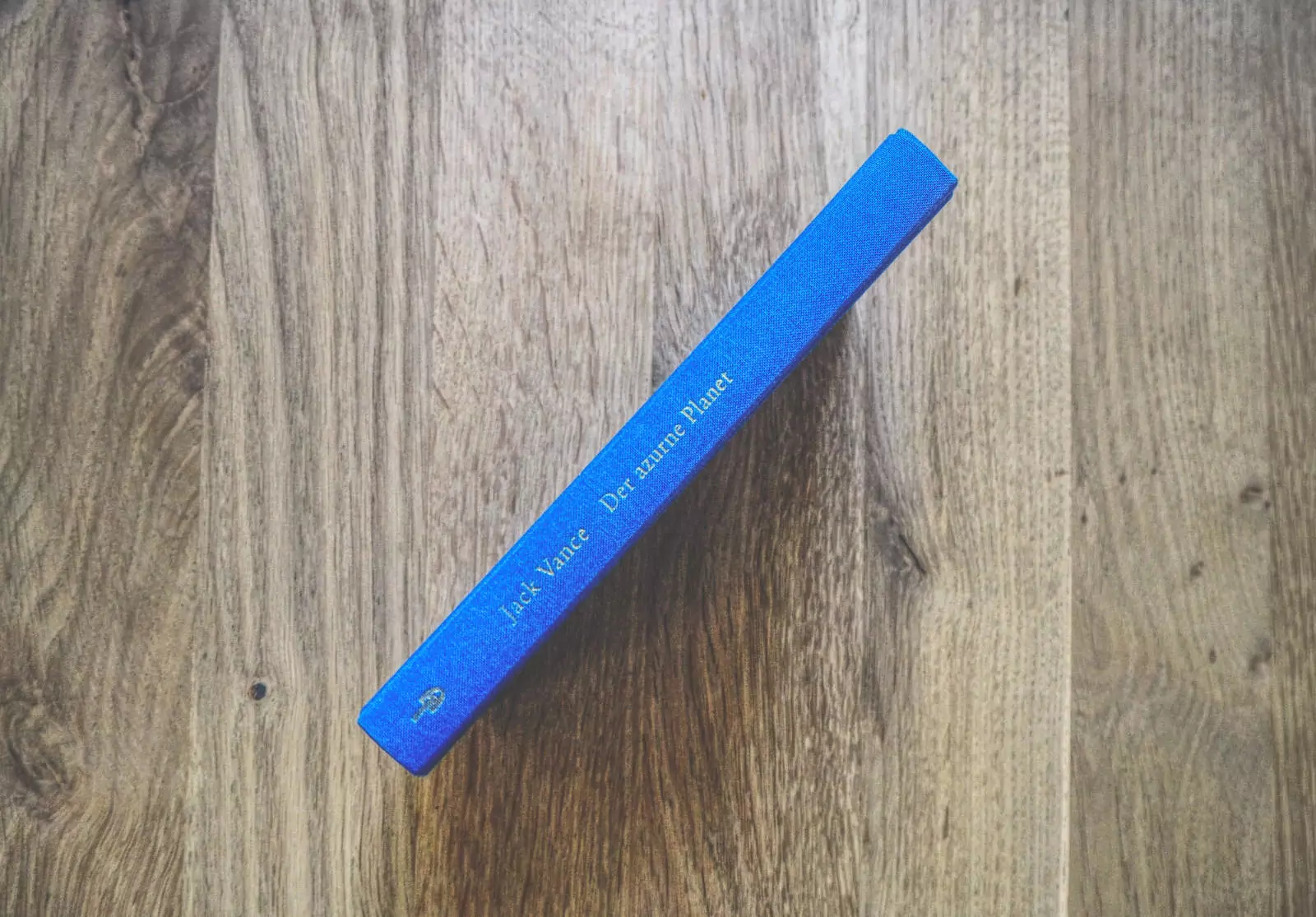 Auf einer Holzfläche liegt ein blaues Buch mit dem Titel „Der blaue Planet“ von Jack Vance.