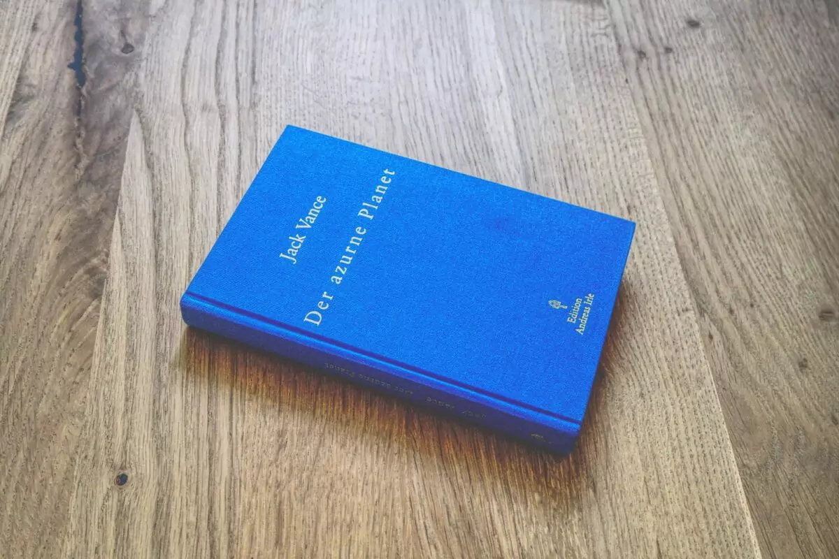 Auf einer Holzfläche liegt ein blaues Hardcover-Buch mit dem Titel „Der azurblaue Planet“ von Jack Vance.