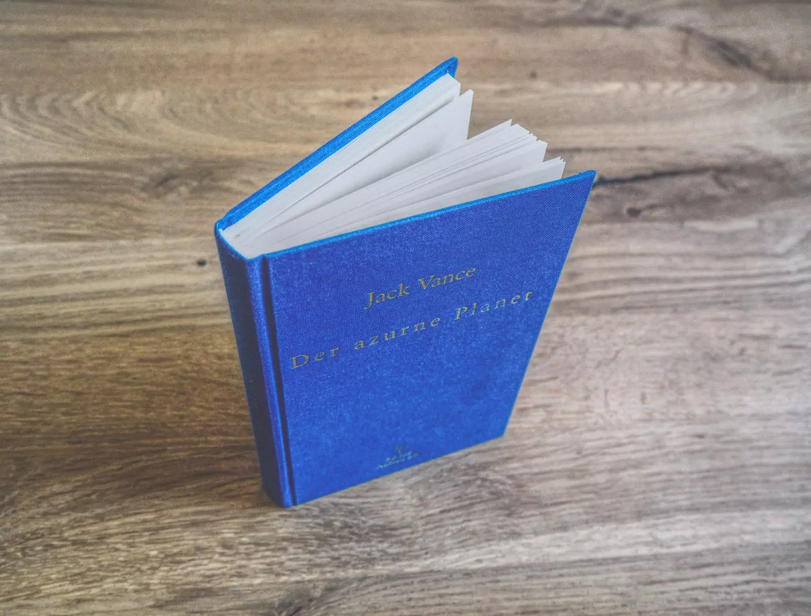 Ein blaues gebundenes Buch mit dem Titel „Der azurne Placer“ von Jack Vance, auf einer Holzoberfläche platziert.
