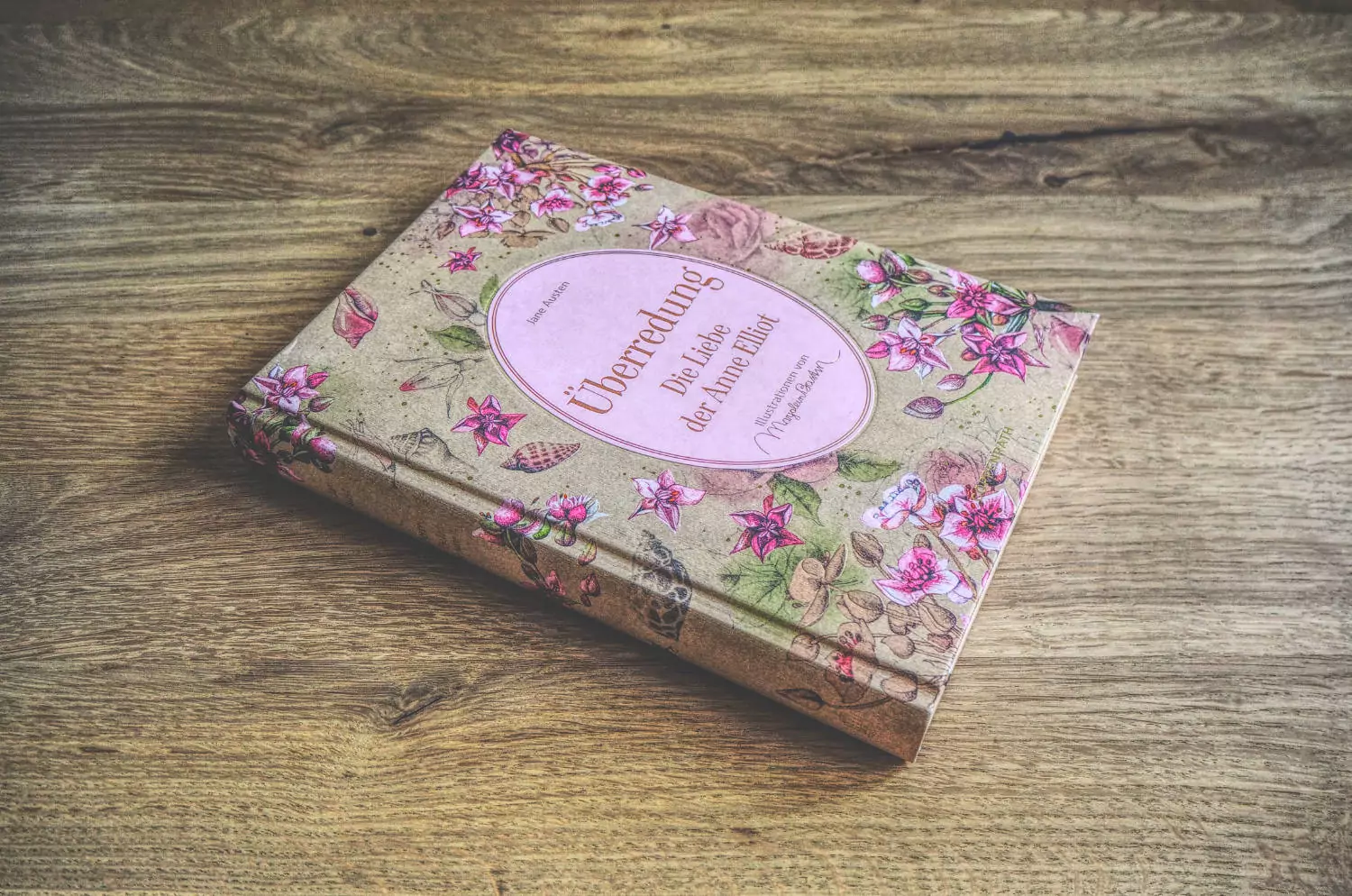Ein Buch mit rosa Blumen auf einem Holztisch.