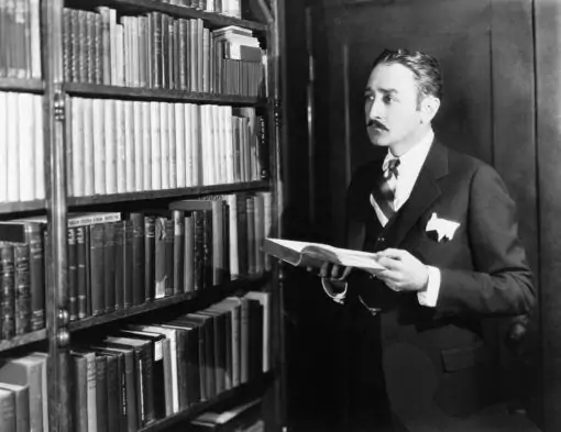 Ein Mann im Anzug steht vor einem Bücherregal.