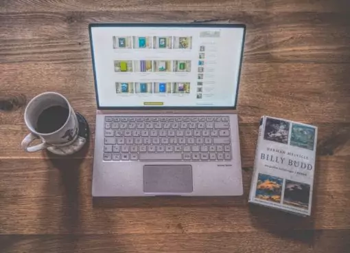 Ein Laptop mit Büchern und einer Tasse Kaffee auf einem Holztisch.