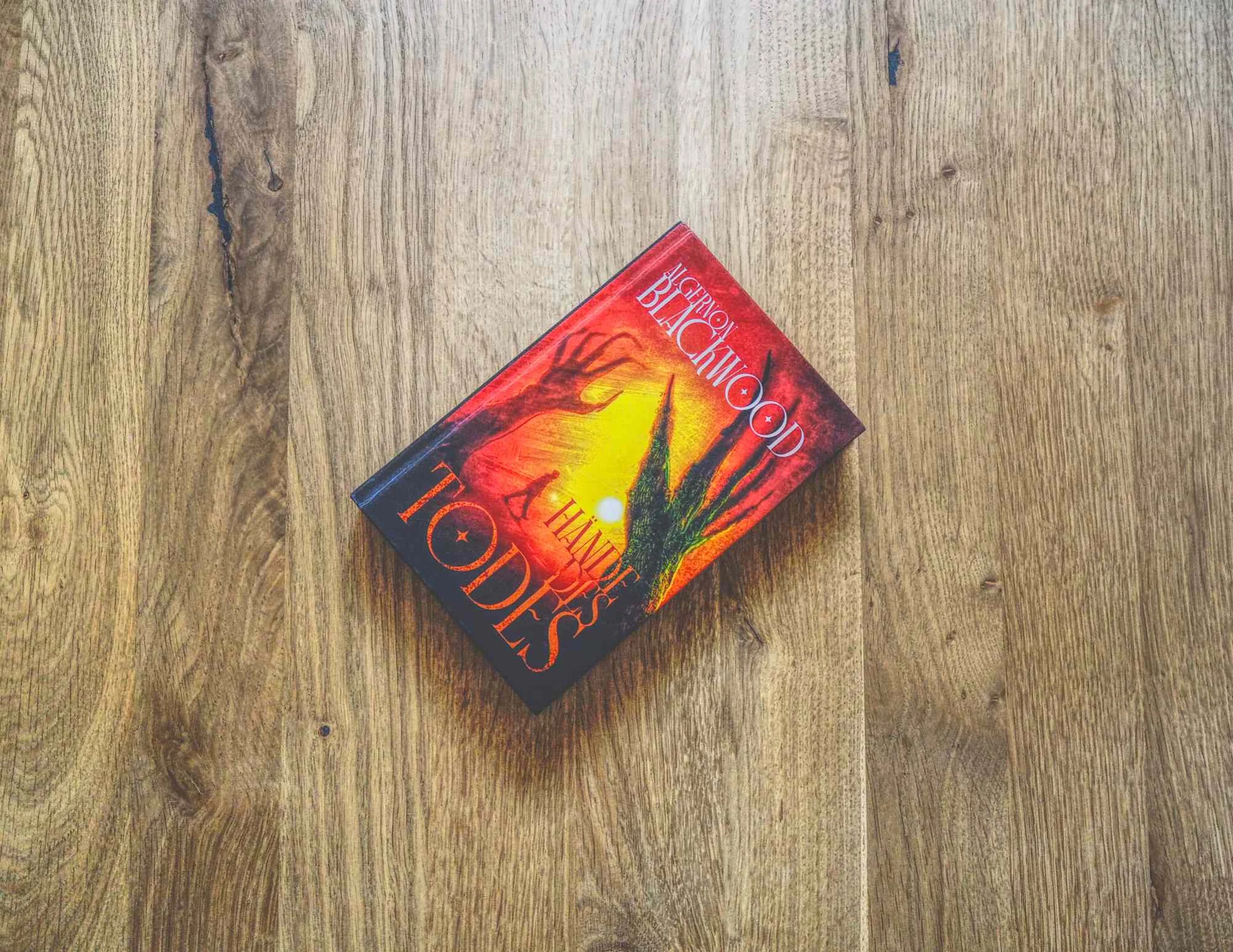 Ein Buch mit dem Titel "Hände des Todes" mit einem illustrierten Einband, der Hände zeigt, die sich nach oben strecken und auf einer hölzernen Oberfläche liegen.