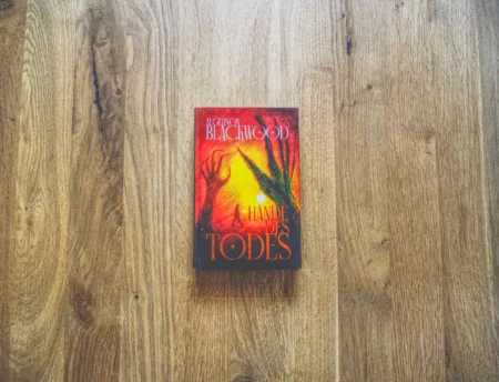 Ein deutsches Buch mit dem Titel "Hände des Todes" von Algernon Blackwood liegt auf einer Holzfläche.