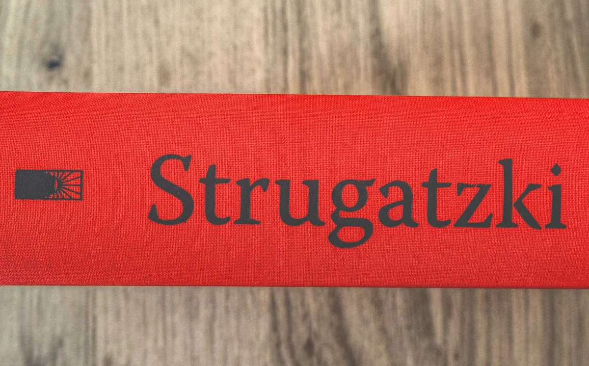Nahaufnahme des Rückens eines roten Buches mit dem schwarzen Text „Strugatzki“ und einem kleinen Logo eines offenen Buches.
