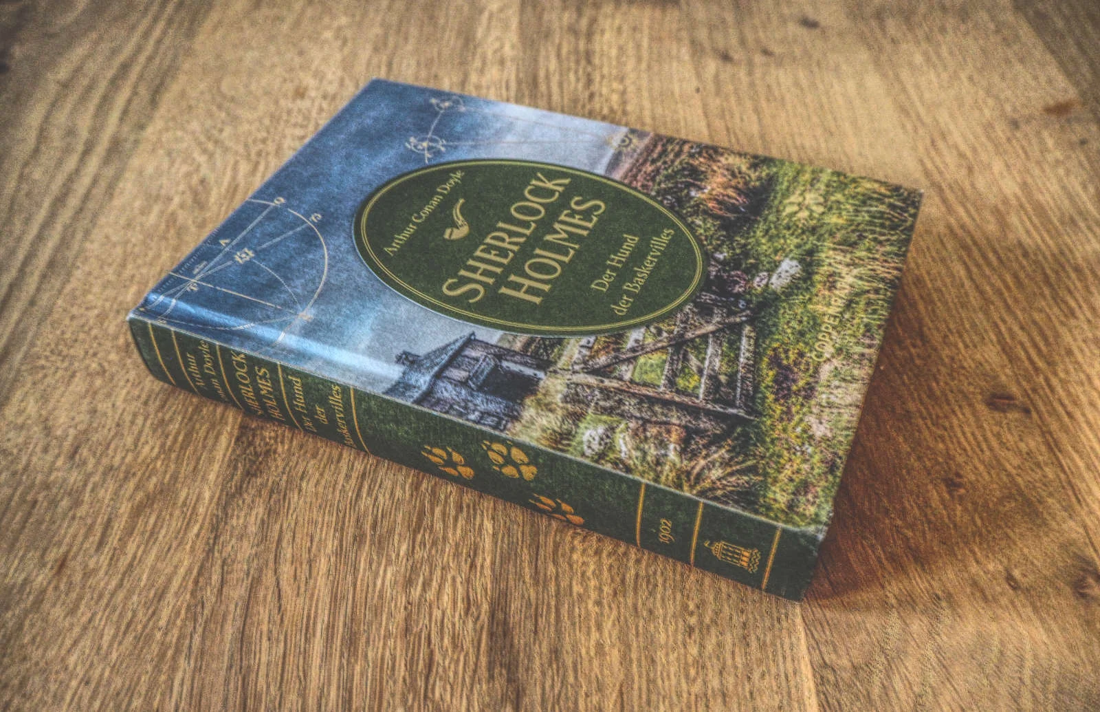 Auf einer Holzoberfläche liegt ein gebundenes Buch mit dem Titel „Sherlock Holmes: Der Hund der Baskervilles“ und einem Cover mit Naturmotiven.