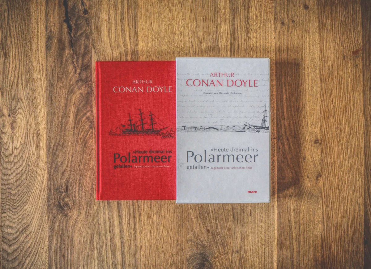 Zwei Bücher von Arthur Conan Doyle auf einer Holzoberfläche. Die Cover sind in deutscher Sprache und unterschiedlich gestaltet. Das rote Buch zeigt eine alte Schiffsillustration und das graue Buch eine Seeszene.