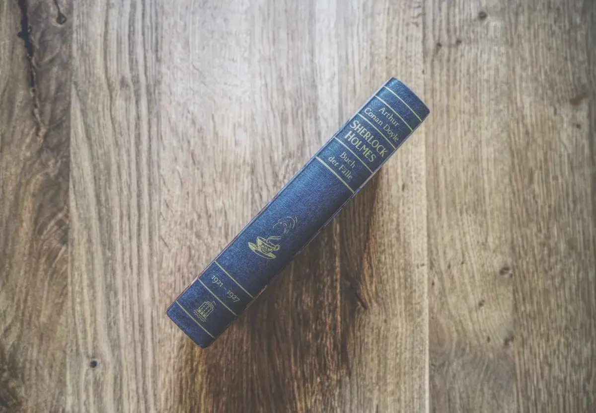 Ein blaues gebundenes Buch mit dem Titel "Sherlock Holmes: Buch der Fälle" von Arthur Conan Doyle liegt auf einer hölzernen Unterlage, die vom Buchrücken aus gezeigt wird.