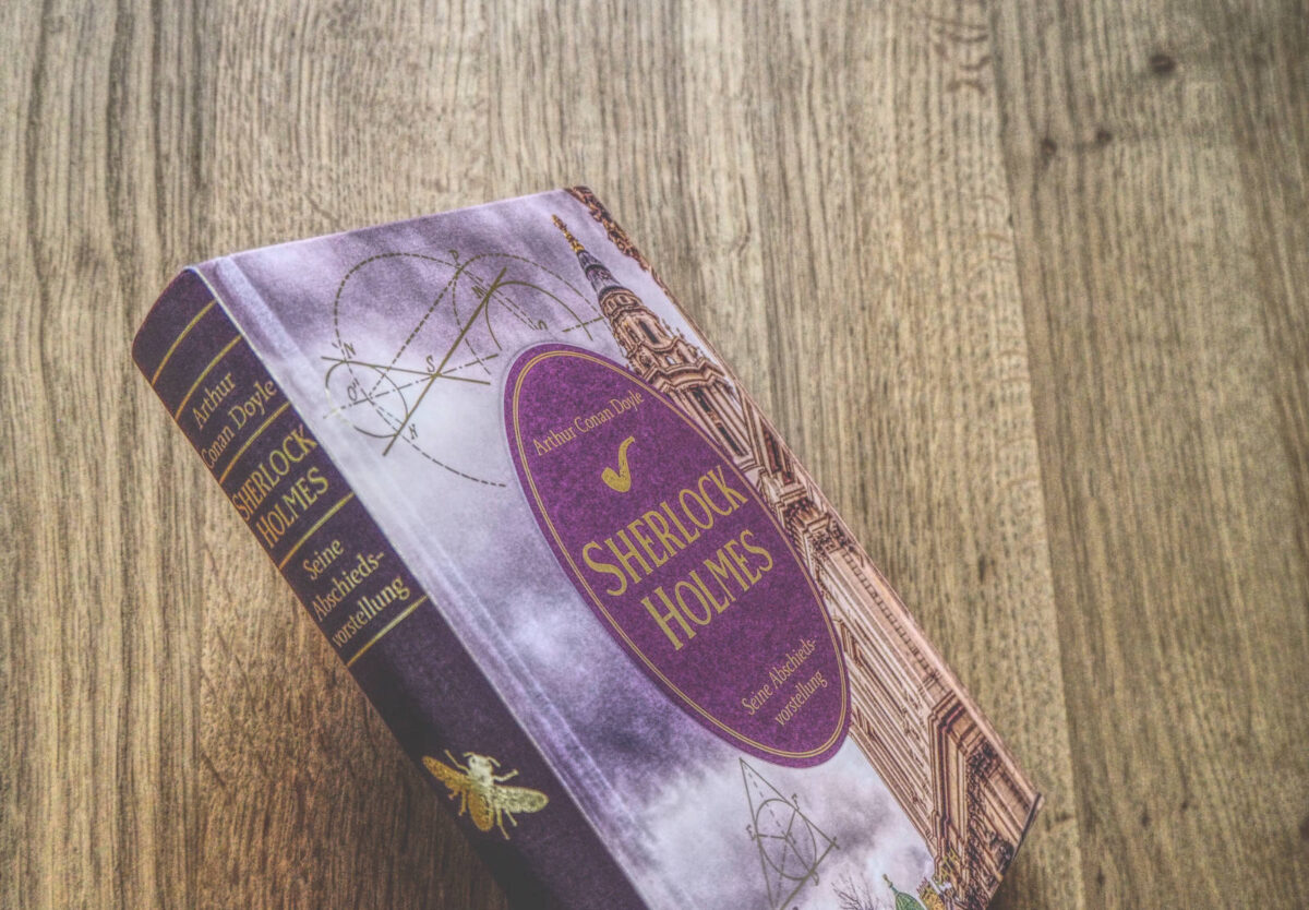 Ein Buch mit violettem Einband liegt auf einem Holztisch.