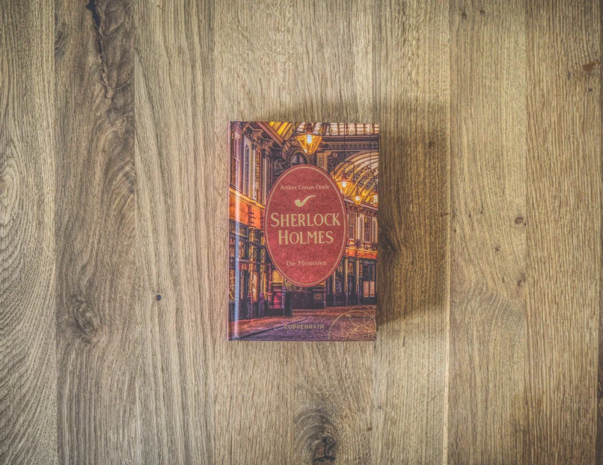 Auf einem Holztisch liegt ein gebundenes Exemplar von „Sherlock Holmes: Die Romane“ von Arthur Conan Doyle mit einem Stadtbild-Cover.