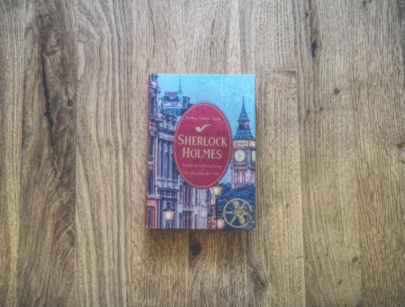 Ein gebundenes Buch mit dem Titel „Sherlock Holmes“ mit historischen Gebäuden und Big Ben im Hintergrund auf einer Holzoberfläche.
