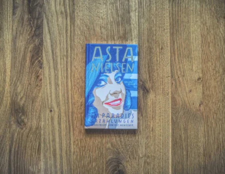 Ein Buch mit dem Titel „Asta Nielsen: Im Paradies Erzählungen“ mit einem illustrierten Porträt auf dem Cover, auf einer Holzoberfläche liegend.