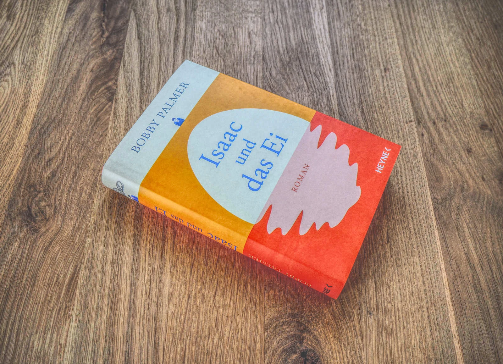 Auf einer Holzfläche liegt ein Buch mit dem Titel „Isaac und das Ei“ von Bobby Palmer.