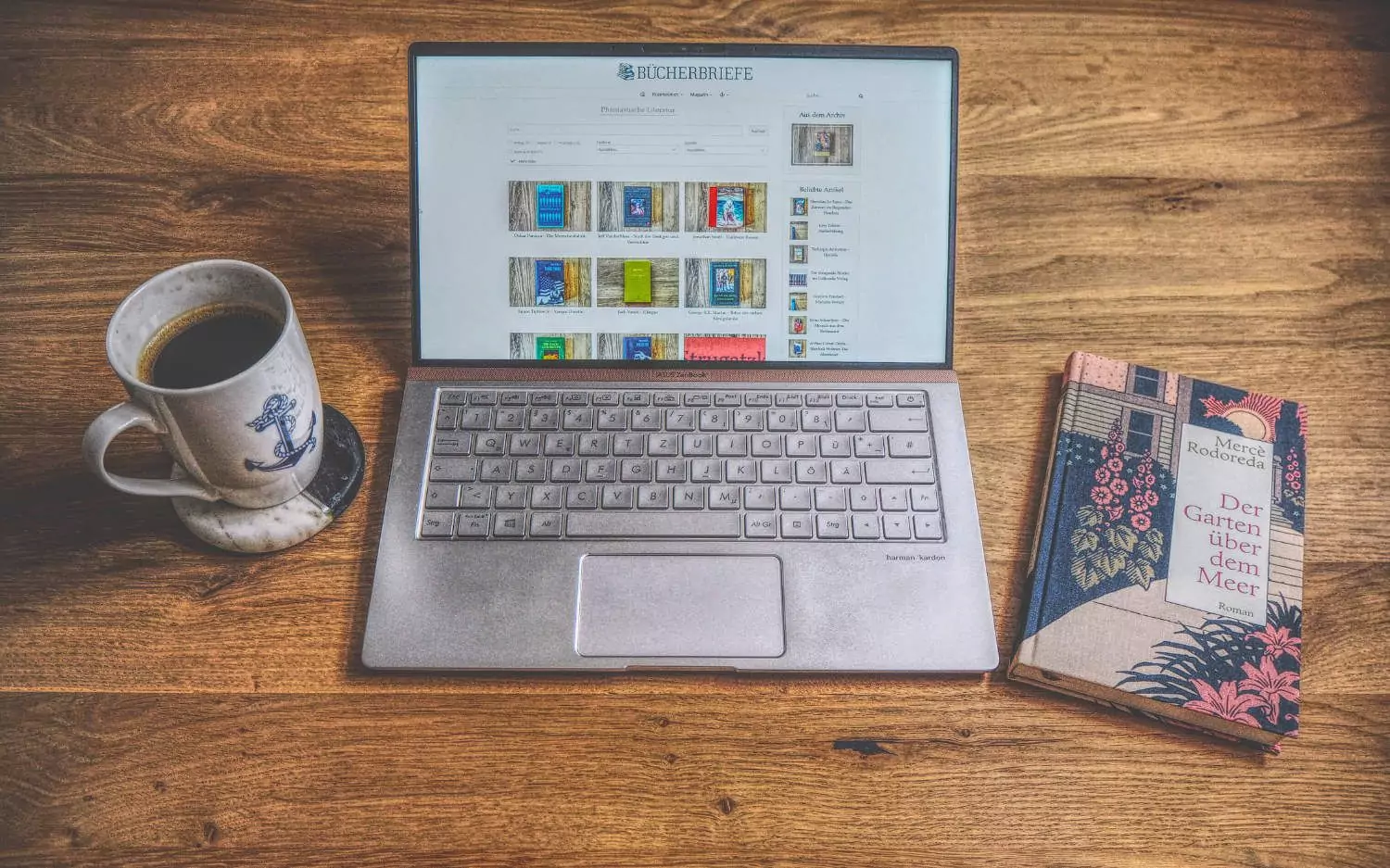 Ein Laptop auf einem Tisch neben einem Buch und einer Tasse Kaffee.