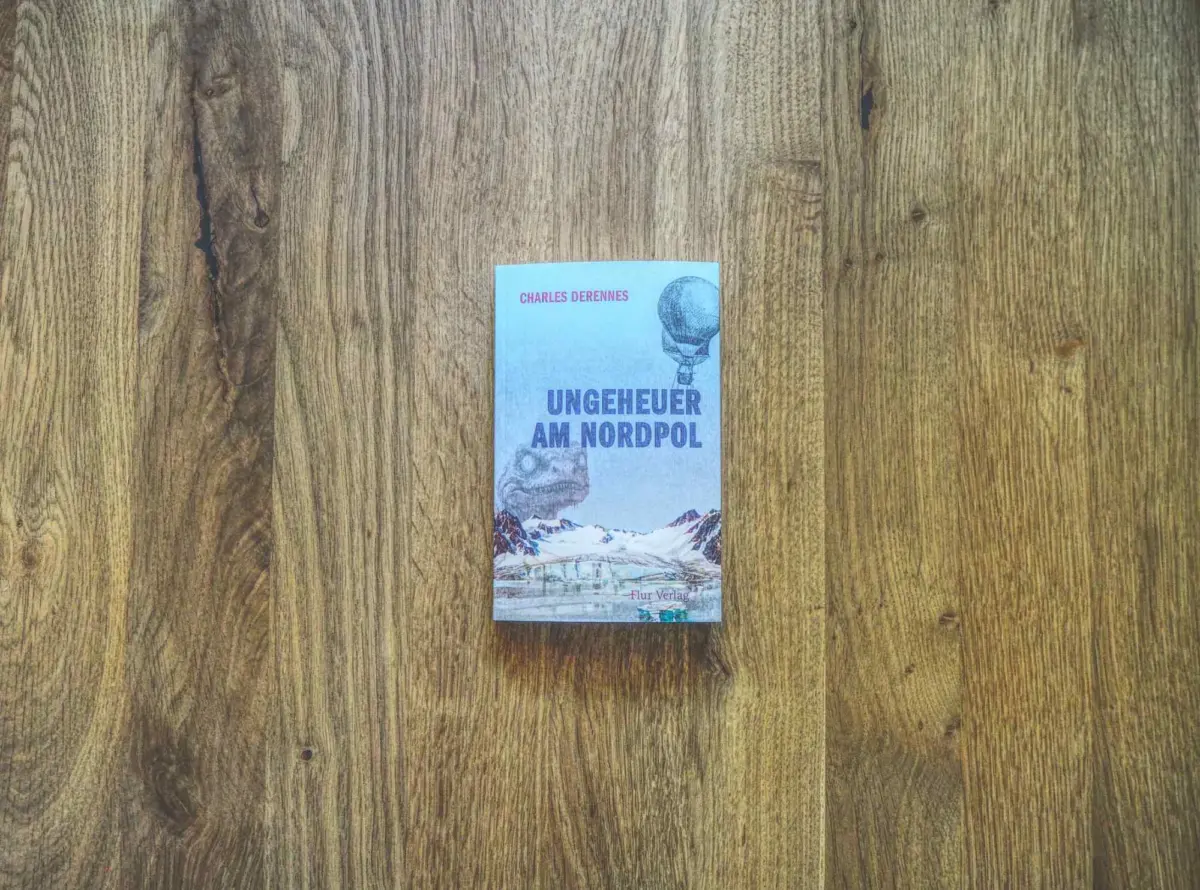 Buch mit dem Titel "Ungeheuer am Nordpol" von Charles Derrennes auf einer Holzoberfläche. Auf dem Einband sind Berge, ein Heißluftballon und eisige Landschaften abgebildet.