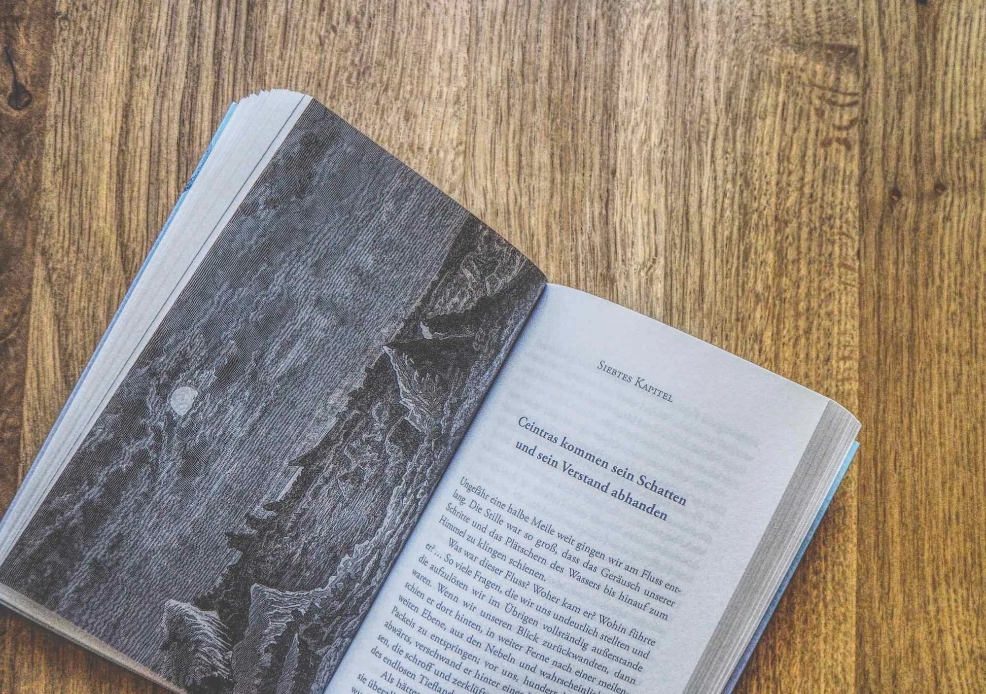 Ein aufgeschlagenes Buch auf einem Holztisch zeigt auf der linken Seite eine Schwarz-Weiß-Illustration und auf der rechten Seite einen deutschen Text mit der Aufschrift "Siebtes Kapitel".