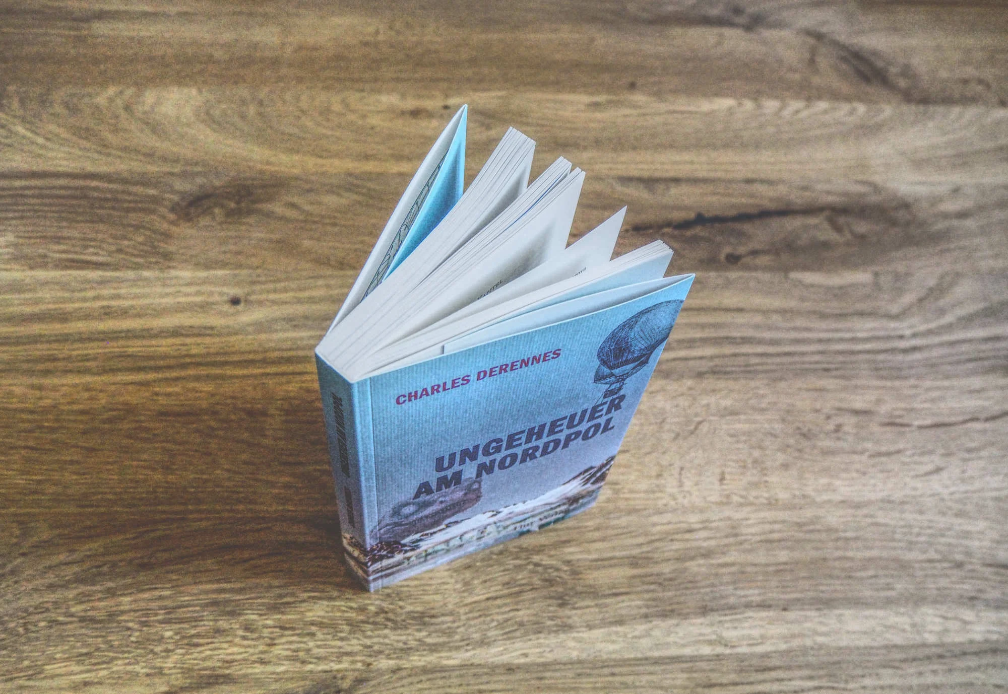 Ein Buch mit dem Titel "Ungeheuer am Nordpol" von Charles Derennes steht aufgeschlagen auf einer Holzplatte.