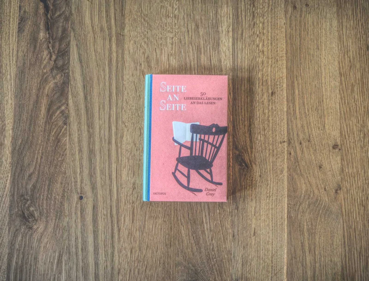 Auf einer Holzfläche liegt ein Buch mit dem Titel „Seite an Seite“, auf dessen Cover ein Schaukelstuhl abgebildet ist.