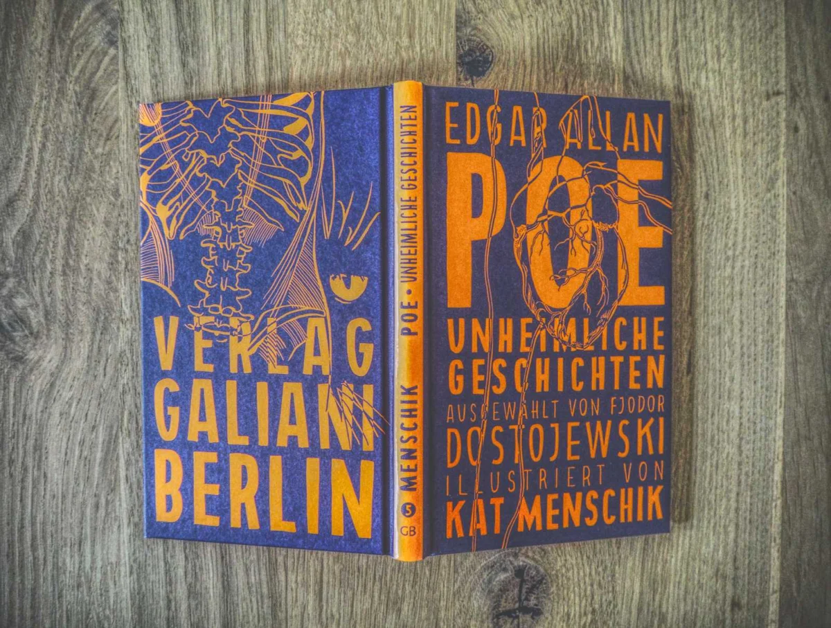 Ein Buch mit einem orange-dunkelblauen Einband mit dem Titel „Unheimliche Geschichten“ von Edgar Allan Poe, illustriert von Kat Menschik, liegt aufgeschlagen auf einer Holzoberfläche.