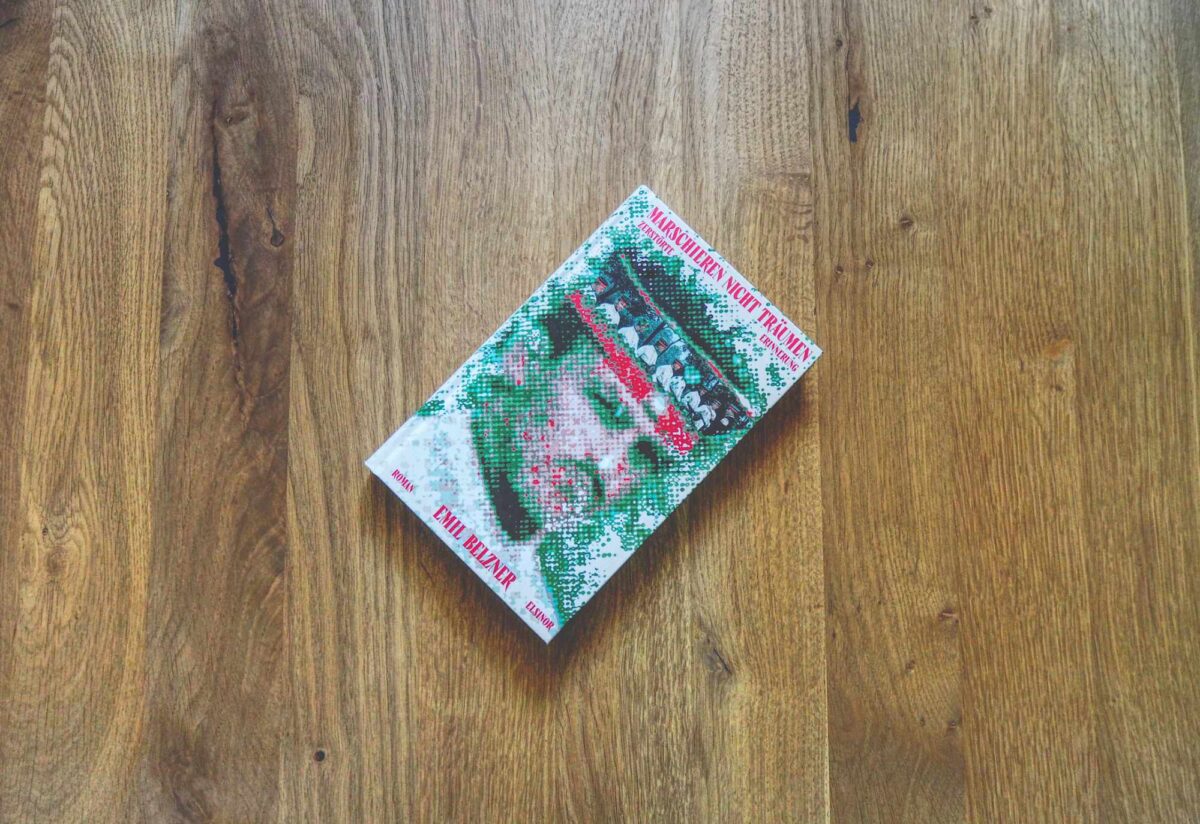 Ein Buch mit dem Titel „Marschieren nicht Träumen“ von Emil Belzner liegt auf einer Holzfläche.