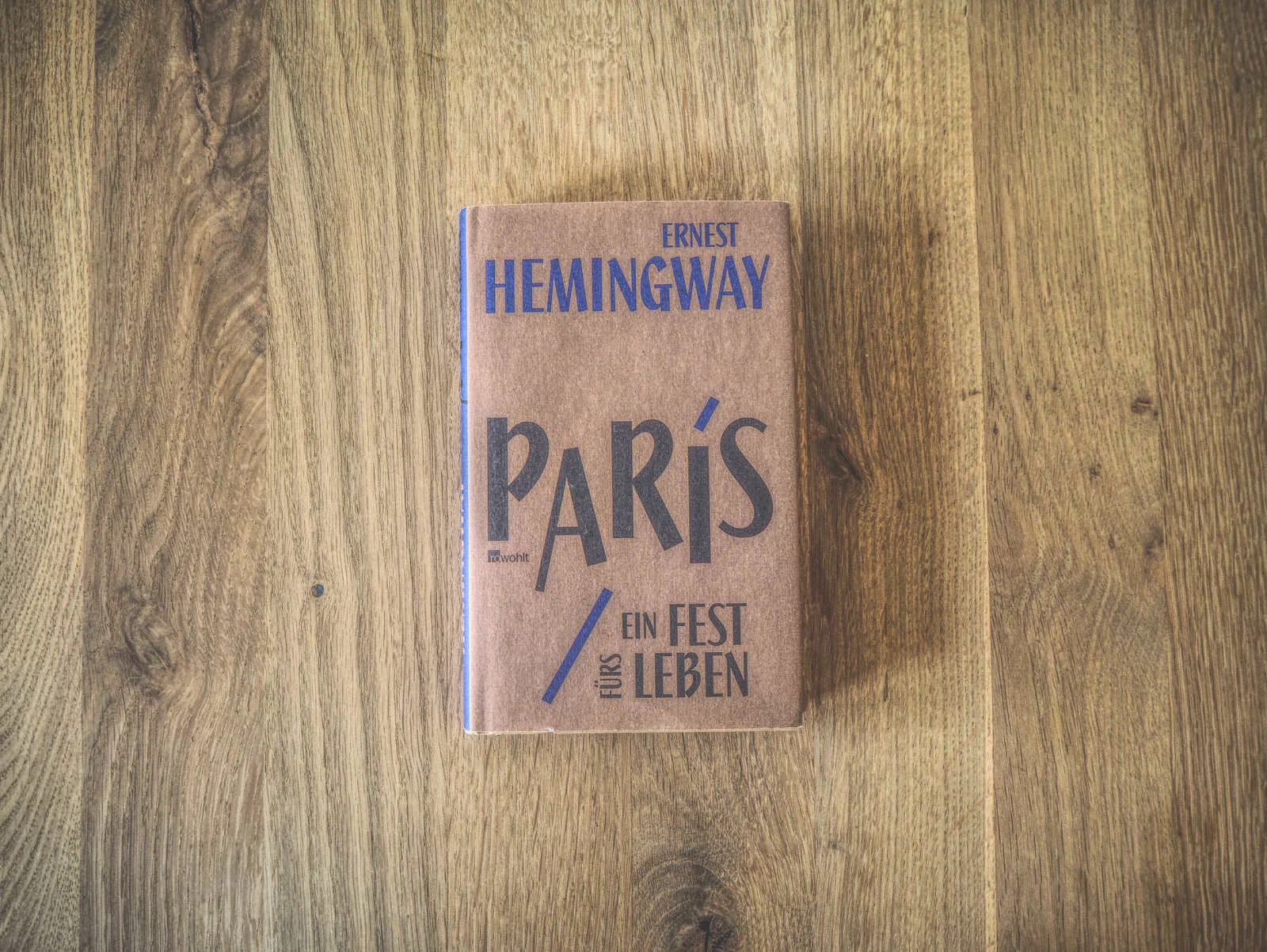 Auf einer Holzunterlage liegt ein Buch mit dem Titel „Paris: Ein Fest fürs Leben“ von Ernest Hemingway.