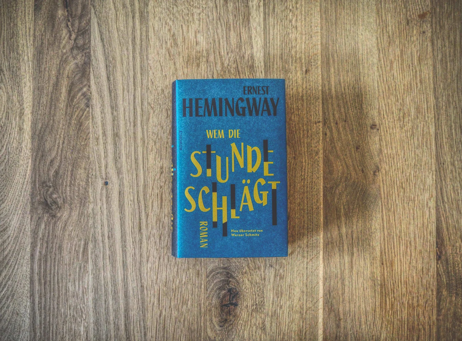 Auf einer Holzfläche liegt eine deutsche Ausgabe des Buches „Wem die Stunde schlägt“ von Ernest Hemingway mit dem Titel „Wem die Stunde schlägt“.