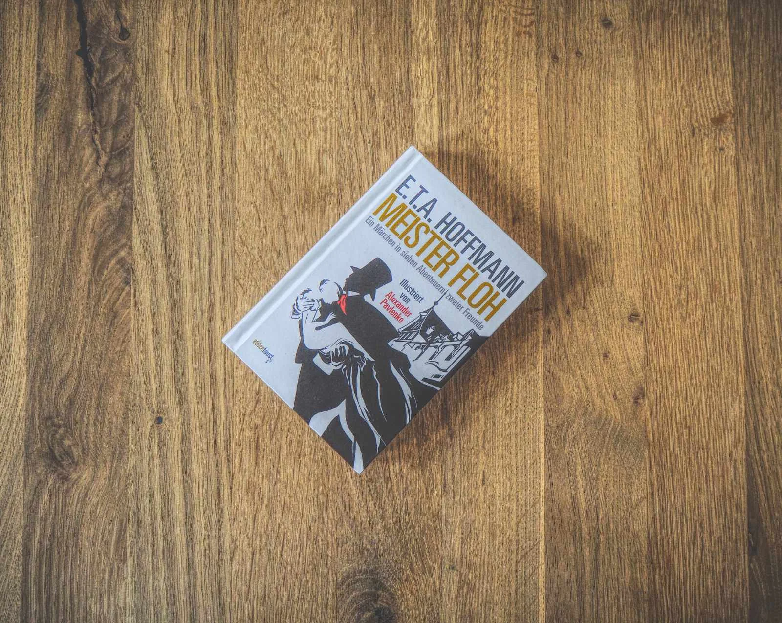Auf einer Holzfläche liegt ein gebundenes Buch mit dem Titel „E.T.A. Hoffmann: Meister Floh“ und illustriertem Cover.