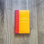 Auf einer Holzfläche liegt ein Buch mit gelbem Einband und dem Titel „Der Spieler“ von Fjodor Dostojewskij.