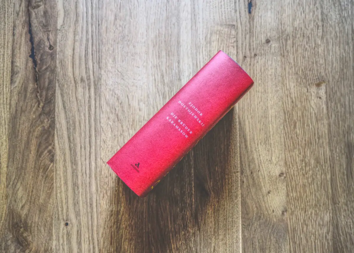 Ein rotes, gebundenes Buch mit Text auf dem Buchrücken liegt von oben betrachtet auf einer Holzfläche.