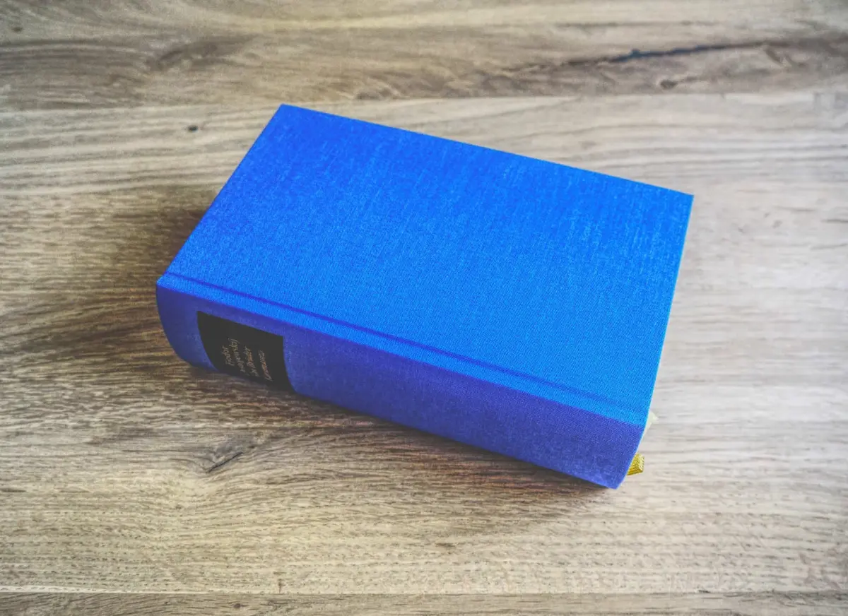 Ein geschlossenes blaues Hardcover-Buch mit einem schwarzen Etikett auf dem Buchrücken ruht auf einer Holzfläche.