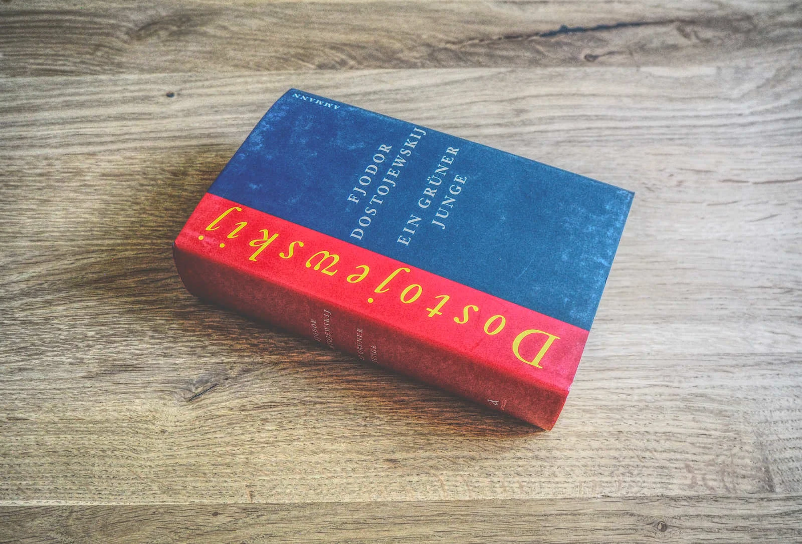 Ein dickes Buch mit dem Titel "Ein grüner Junge" von Fjodor Dostojewski liegt auf einer Holzplatte.