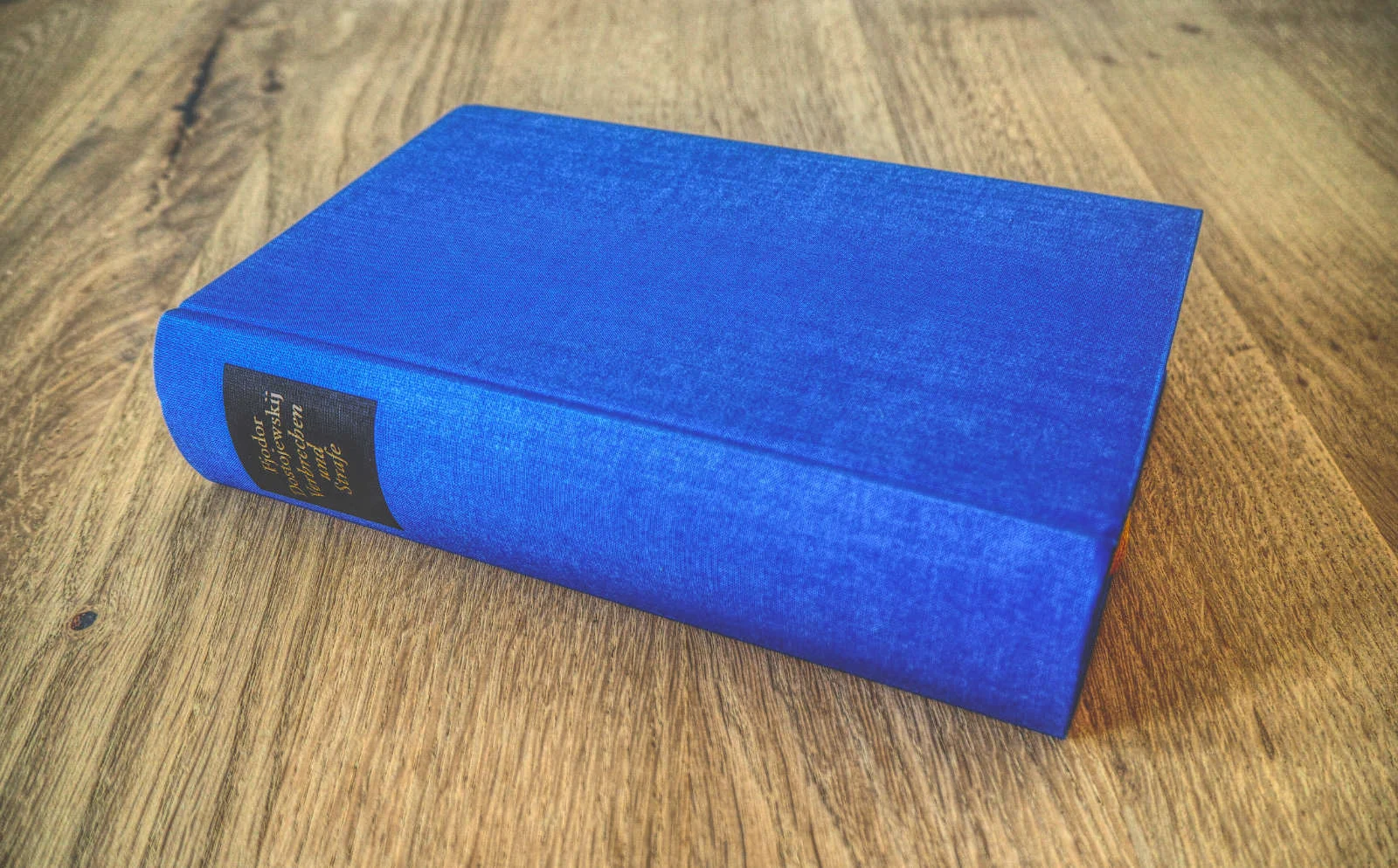 Ein blaues Hardcover-Buch liegt geschlossen auf einer Holzoberfläche.