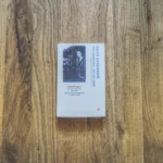 Auf einer Holzfläche liegt ein Buch mit dem Titel „Das Schicksal der Salome“ von Gaito Gasdanow. Auf dem Cover ist ein altes Foto eines Mannes zu sehen, der neben einem Auto steht.