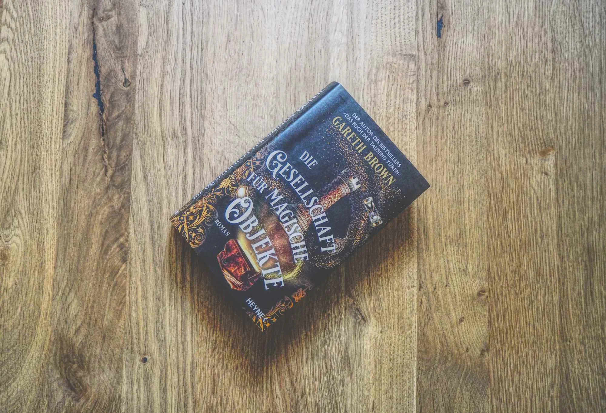 Ein deutsches Buch mit dem Titel "Die Gesellschaft für Magische Antiquitäten" von Gareth F. Brown liegt auf einer Holzfläche.