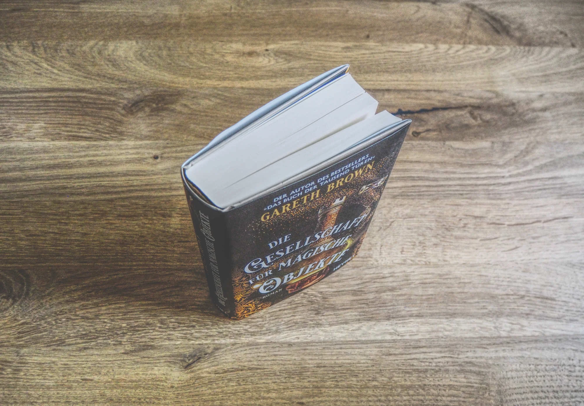 Ein gebundenes Buch mit dem Titel "Die Gesellschaft der magischen Erleuchtung" von Gareth Brown liegt aufrecht auf einer Holzfläche.