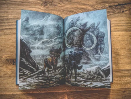 Aufgeschlagenes Buch auf einem Holztisch. Das Buch zeigt eine Illustration von drei Tieren, die ein großes, mystisches Wesen in einer verschneiten Berglandschaft betrachten.