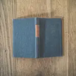 Ein altes gebundenes Buch mit grünem Einband und braunem Buchrücken und dunklem Text liegt aufgeschlagen auf einer Holzoberfläche. Der Titel des Buches ist nicht zu sehen.