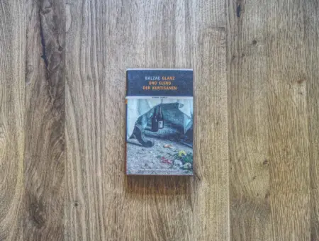 Ein Buch mit dem Titel "Balzac Glanz und Elend der Kurtisanen" liegt geschlossen auf einer Holzplatte.