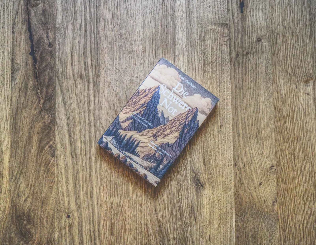 Auf einer Holzfläche liegt ein Buch mit dem Titel „Die Schwere Not“, auf dem Cover ist eine Berglandschaft abgebildet.