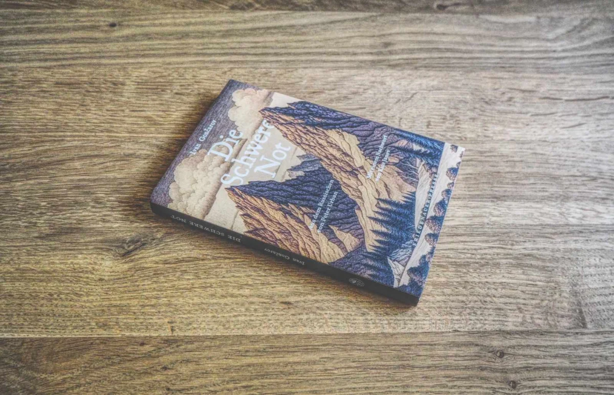 Auf einer Holzfläche liegt ein Buch mit dem Titel „Die Schwere Not“ und einem illustrierten Berg-Cover.