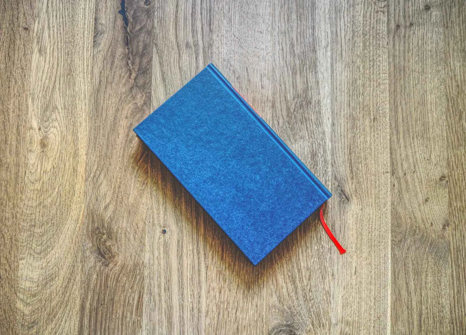 Ein geschlossenes blaues Buch mit einem Lesezeichen mit roter Schleife liegt auf einer Holzfläche.
