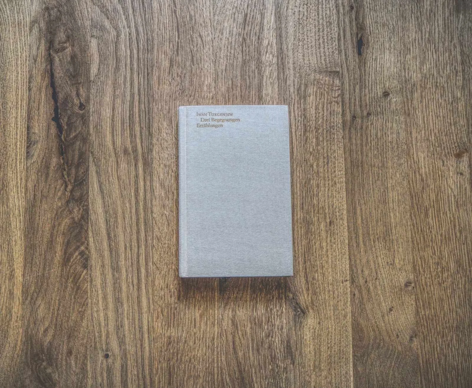 Ein beiges Hardcover-Buch liegt geschlossen auf einem Holztisch.