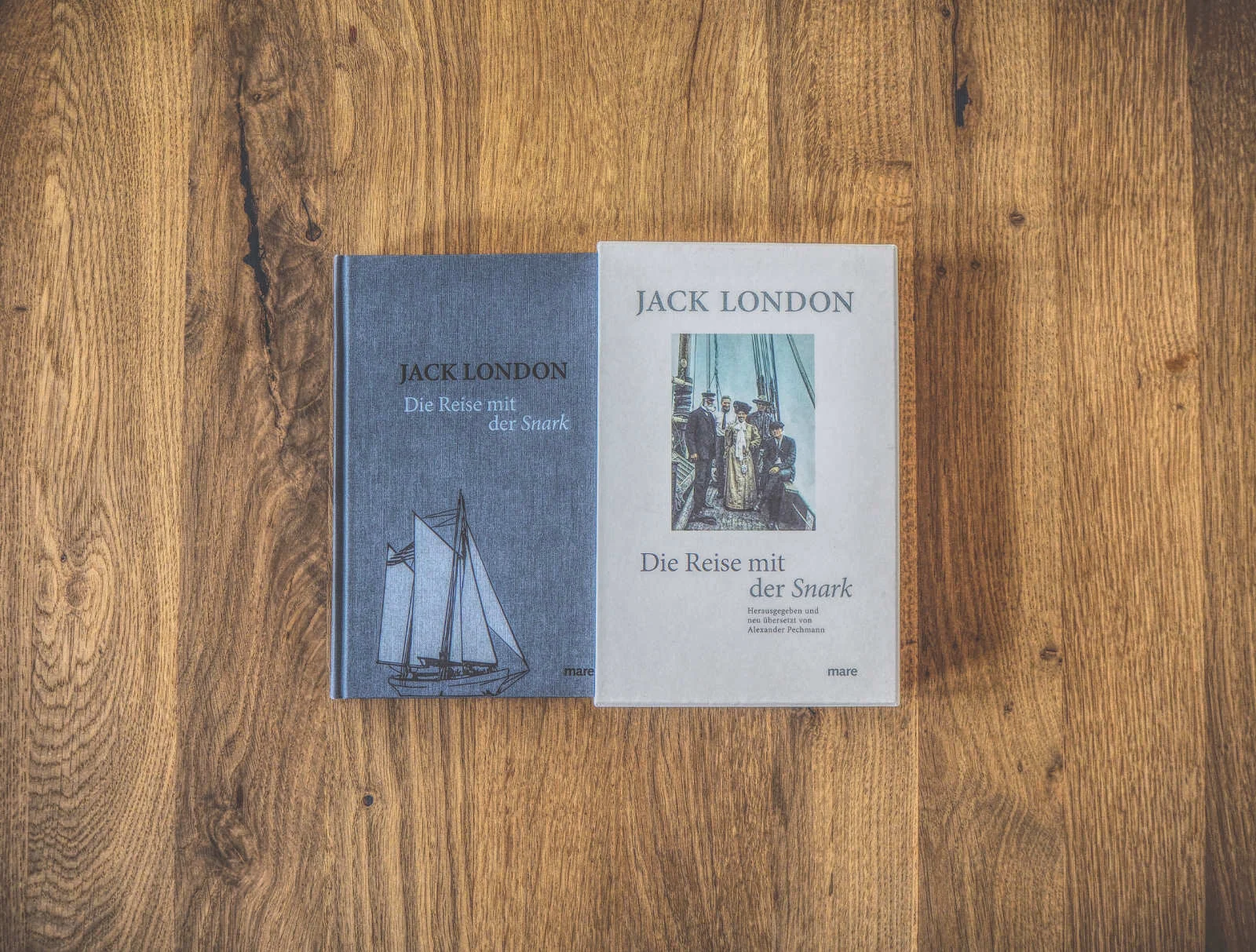 Zwei Bücher mit dem Titel „Die Reise mit der Snark“ von Jack London liegen nebeneinander auf einer Holzfläche. Ein Buch hat einen blauen Einband mit der Zeichnung eines Segelboots, das andere einen weißen Einband.